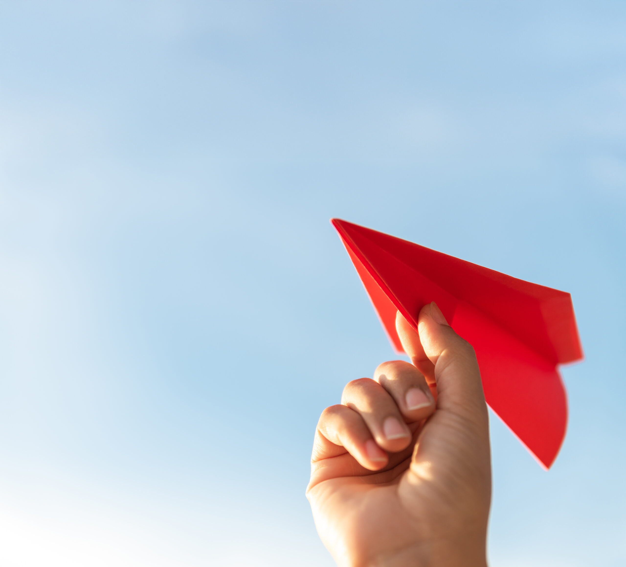 Woman Hand holding red paper rocket with blue sky background. freedom concept.