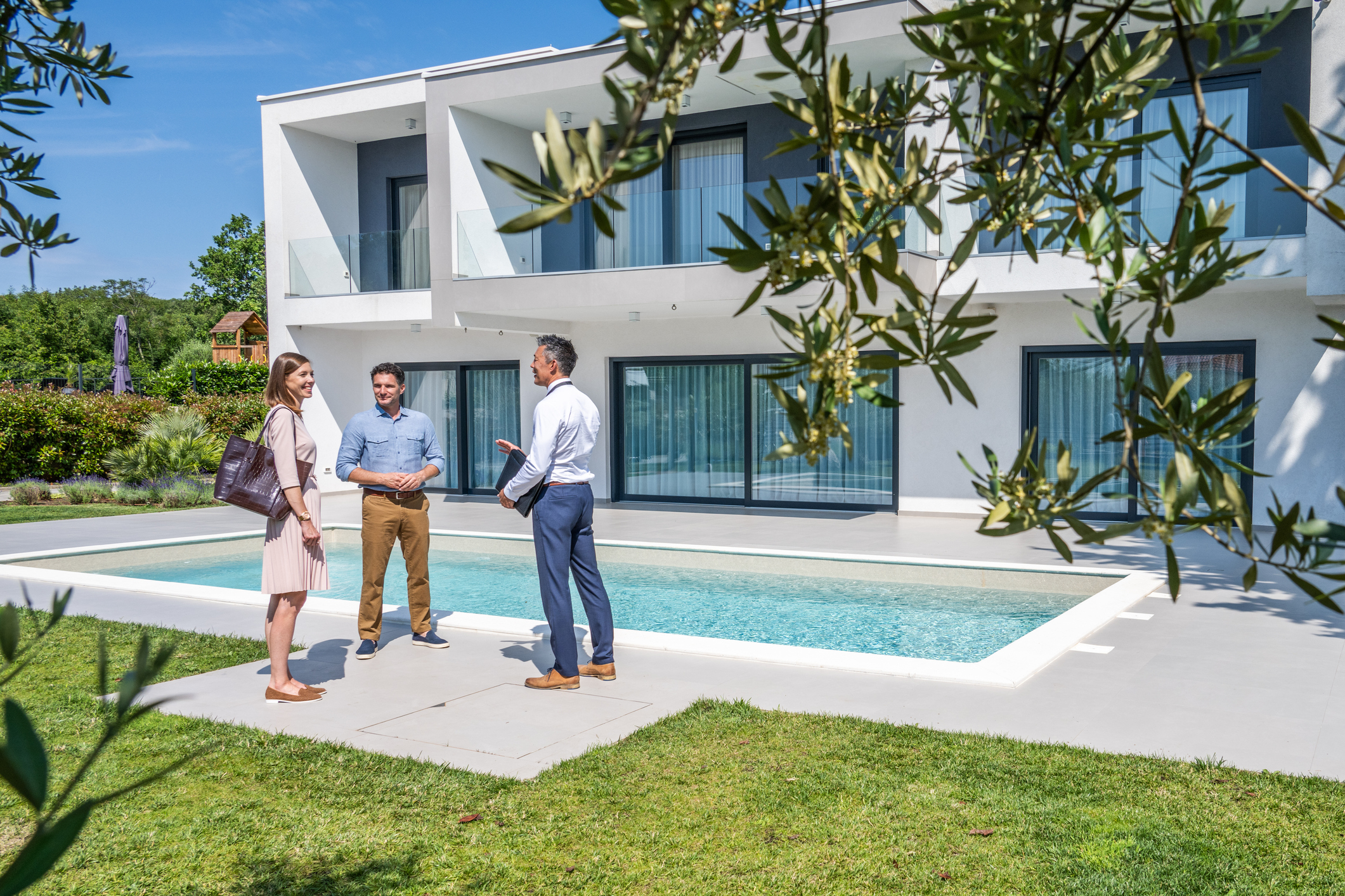 Male real estate agent talking with couple Paar mit einem Immobilienmakler im Garten einer Villa mit Pool
