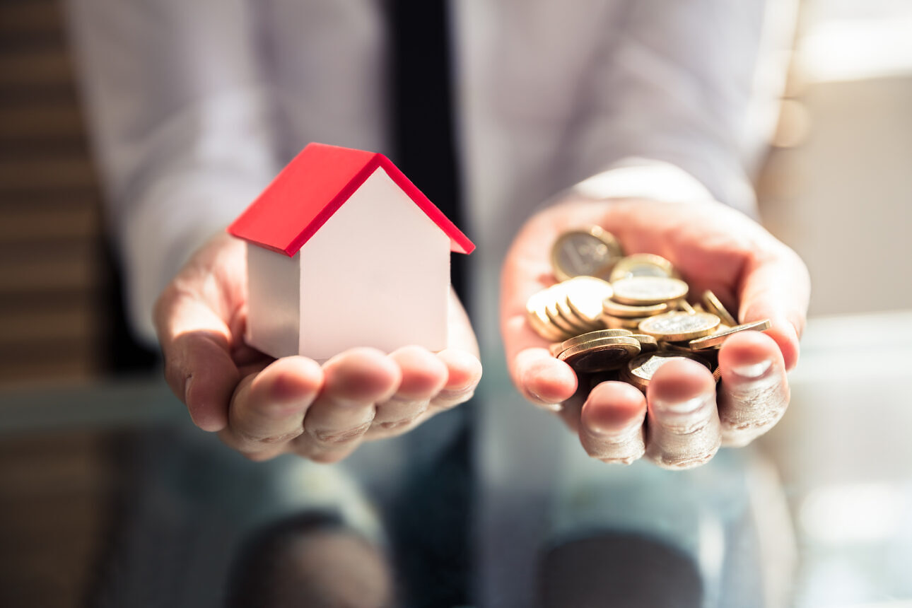 Businessperson Holding House Model And Golden Coins Eigentumswohnung verkaufen